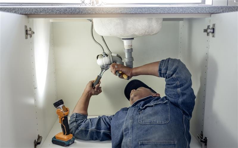 Plumber repairing pipes beneath a bathroom sink in Rome