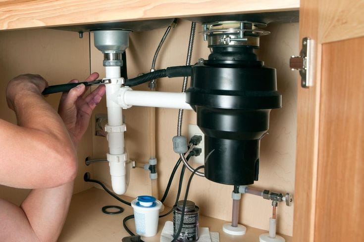 Plumber installing a garbage disposal beneath a kitchen sink in Rome