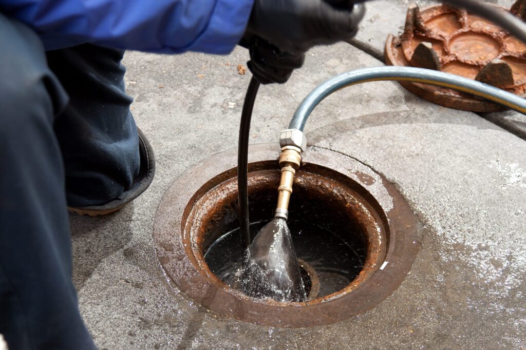 Plumber hydro jetting a sewer line through a manhole in Rome