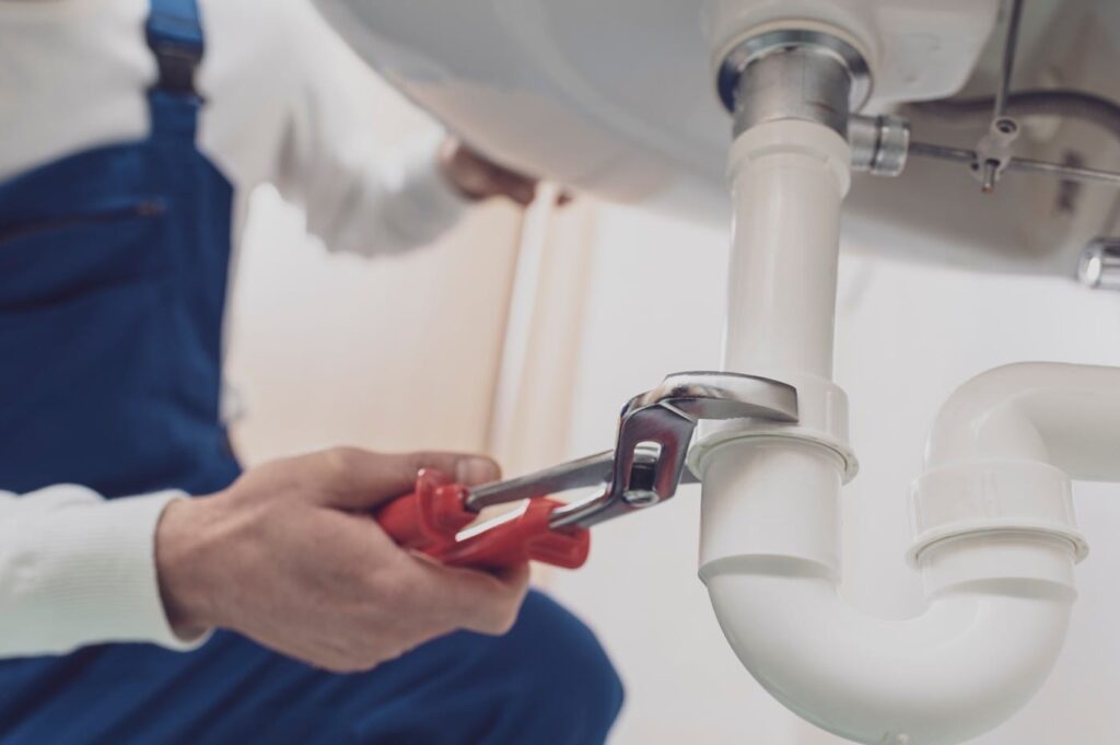 Plumber repairing a white drain pipe beneath a sink in Rome